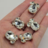 Bright gold 2 hole slider beads with brilliant Clear faceted rhinestones for handmade jewelry making. Each decorative focal features a large teardrop-shaped crystal accented by two smaller coordinating rhinestones. Measuring approximately 20 mm long and 16 mm wide, these sparkling jewelry connectors are ideal for double-strand bracelets, necklaces, bead weaving, bridal designs, formal jewelry, and elegant handmade accessories.