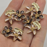 Floral enamel 2 hole slider beads in a polished bright gold finish with blush pink, deep plum, and ivory botanical accents. These dimensional 26 mm focal beads feature two coordinating flowers and a sculpted leaf arranged like a miniature bouquet. Dual stringing holes help position the decorative bead in double-strand bracelets, multi-strand jewelry, necklaces, bead weaving, botanical accessories, and romantic handmade jewelry projects.