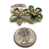 Dimensional green flower slider beads in bright gold plated metal featuring deep emerald, soft sage, and pearly ivory enamel details. These 2 hole focal beads create a decorative botanical centerpiece for bracelets, necklaces, multi-strand jewelry, and bead weaving designs. The sculpted flowers and leaf add texture, color, and elegant garden-inspired detail to handmade jewelry projects and artisan bracelet designs.