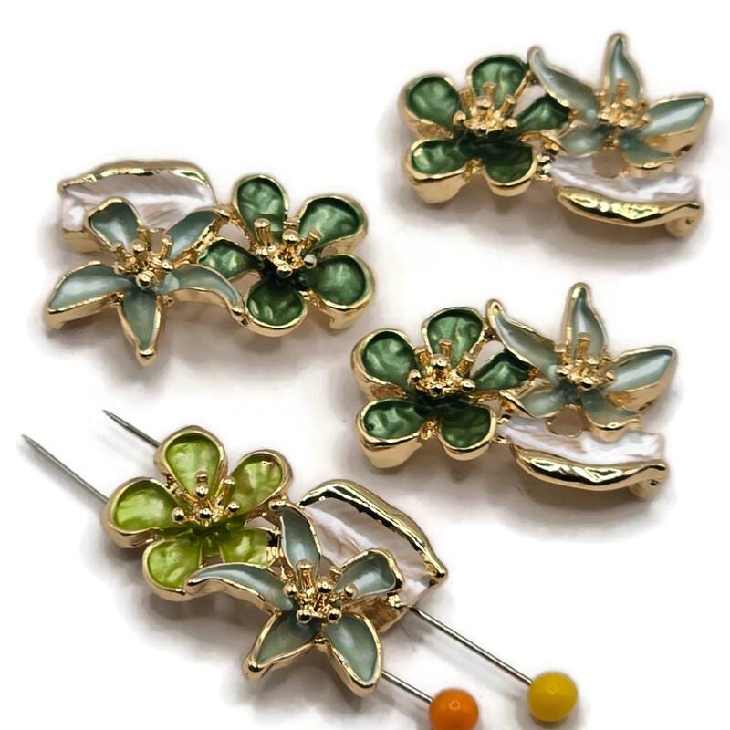 Green floral 2 hole slider beads featuring emerald and sage enamel flowers with pearly ivory leaves and bright gold metal detailing. These dimensional botanical focal beads have two side holes for double-strand bracelets, necklaces, bead weaving, and handmade jewelry designs. Decorative flower connector beads combine rich green enamel, soft natural tones, and polished gold for elegant garden-inspired jewelry making projects.