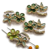 Green floral 2 hole slider beads featuring emerald and sage enamel flowers with pearly ivory leaves and bright gold metal detailing. These dimensional botanical focal beads have two side holes for double-strand bracelets, necklaces, bead weaving, and handmade jewelry designs. Decorative flower connector beads combine rich green enamel, soft natural tones, and polished gold for elegant garden-inspired jewelry making projects.