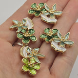 Bright gold floral 2 hole slider beads with dimensional emerald green and sage enamel flowers accented by a pearly ivory leaf. These botanical jewelry connectors measure approximately 26 mm long and feature 7.5 mm spacing between the holes. Beautiful focal beads for double-strand bracelets, bead weaving, necklaces, cuffs, handmade jewelry, nature-inspired designs, and jewelry making at home.
