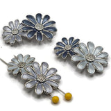 Mixed blue double-daisy 2 hole slider beads featuring coordinating enamel flowers in a platinum silver, stainless-steel-colored finish. Each floral focal bead combines two connected daisy designs with textured silver centers and soft blue, gray-blue, and deeper slate-blue enamel petals. Decorative jewelry-making components for double-strand bracelets, bead weaving, handmade necklaces, floral jewelry designs, DIY bracelet making, spring jewelry, and creative jewelry making at home.