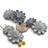 Double-daisy floral 2 hole slider beads in three coordinating blue enamel color combinations with platinum silver metal accents. Each jewelry focal bead features two connected flowers with elongated enamel petals and detailed textured centers. The cool stainless-steel-colored finish complements the soft blue, silvery blue, and dark slate tones beautifully. Unique jewelry-making supplies for beaded bracelets, necklaces, bead weaving, multi-strand jewelry, handmade jewelry, and botanical.