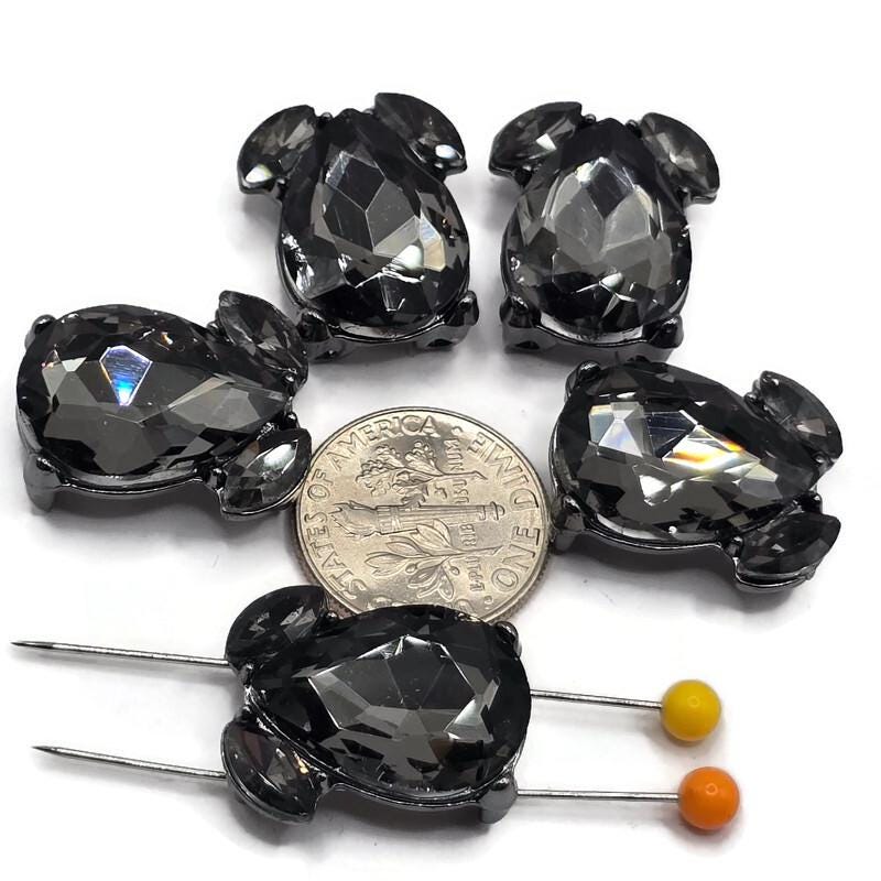 Gunmetal 2 hole slider beads featuring large faceted Black Diamond teardrop rhinestones with two smaller coordinating crystal accents. Each 20 mm focal bead has two hidden stringing loops on the back, approximately 9 mm apart, for double-strand jewelry designs. Smoky gray rhinestones and dark gunmetal metal create dramatic sparkle for handmade bracelets, necklaces, bead weaving, statement jewelry, and creative jewelry-making projects.