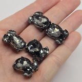 Black Diamond rhinestone 2 hole slider beads in a dark gunmetal plated metal finish for handmade jewelry making. Large faceted teardrop crystals are accented with two smaller smoky rhinestones for dimensional sparkle. Measuring approximately 20 mm long and 16 mm wide, these statement focal beads feature hidden back loops for double-strand bracelets, multi-strand necklaces, bead weaving, cuffs, and sophisticated DIY jewelry designs.