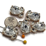 Clear faceted rhinestone focal beads in a polished bright gold finish featuring two hidden back loops for jewelry making. Each 20 mm slider bead combines a large teardrop-shaped crystal with two smaller coordinating stones for dimensional sparkle. Elegant 2 hole jewelry components for double-strand bracelets, multi-strand designs, bead weaving, bridal jewelry, necklaces, holiday accessories, and sparkling handmade jewelry creations.