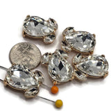 Gold and Clear rhinestone 2 hole slider beads designed for sparkling handmade bracelets and jewelry. Each focal bead features a brilliant faceted teardrop crystal surrounded by two smaller Clear rhinestones in a warm bright gold setting. Two discreet stringing loops on the back help position these statement components in double-strand bracelets, bead weaving, necklaces, bridal accessories, and elegant jewelry-making designs.