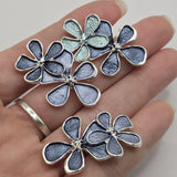 Beautiful bright silver floral focal beads featuring rich smoky blue enamel flowers and a delicate aqua accent blossom. These decorative 2 Hole Slider Beads showcase three overlapping five-petal flowers with polished silver outlines and raised decorative centers. Perfect for handmade jewelry designs, multi-strand bracelets, necklace making, and bead weaving projects. Unique jewelry findings for feminine floral jewelry, thoughtful handmade gifts, and elegant blue jewelry collections.