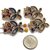Beautiful multicolor floral 2 Hole Slider Beads featuring three overlapping flowers with rich charcoal gray, smoky champagne, burgundy, purple, and navy blue enamel petals. Each decorative jewelry focal bead features bright reflective gold outlines and a delicate openwork gold flower accent. This coordinated assortment is perfect for handmade bracelets, necklace designs, bead weaving, and multi-strand jewelry. Unique jewelry making supplies for elegant floral accessories