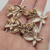 Elegant bright gold flower jewelry making beads featuring layered floral designs with contrasting champagne brown, pearly ivory, and chocolate brown enamel petals. Each 2 Hole Slider Bead showcases a large decorative flower paired with a smaller contrasting blossom and delicate openwork gold floral accents. Beautiful jewelry components for bracelet making, necklace designs, bead weaving, and handmade accessories.