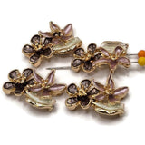 Stunning bright gold Flower Slider Beads showcasing an artistic arrangement of overlapping enamel blossoms in smoky brown, muted mauve, and pearly ivory. Each decorative jewelry component features rounded flower petals, raised gold floral centers, and a graceful curved leaf accent. These dimensional 2 Hole Slider Beads are perfect for handmade bracelets, beaded necklaces, multi-strand jewelry, and creative bead weaving.