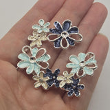 Beautiful bright silver floral 2 Hole Slider Beads featuring three overlapping flowers in soft light blue, deep navy blue, and pearly ivory enamel. Each decorative jewelry focal bead showcases dimensional blossoms with textured enamel petals, reflective silver outlines, and delicate openwork flower details. These unique jewelry making components are perfect for handmade bracelets, necklace designs, bead weaving, and multi-strand jewelry.