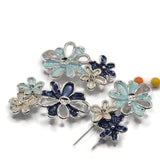 Stunning bright silver Flower Slider Beads showcasing an artistic arrangement of overlapping blossoms in pale aqua blue, deep midnight blue, and luminous ivory enamel. Each decorative jewelry component features dimensional flower petals, polished silver outlines, and delicate openwork metallic accents. These unique 2 Hole Slider Beads are perfect for handmade bracelets, beaded necklaces, multi-strand jewelry, and creative bead weaving.