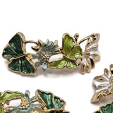 Package of four bright gold butterfly and floral slider beads featuring colorful dark green and lime green butterflies with delicate white and muted sage flowers. The textured enamel wings are outlined in reflective gold, while dimensional floral accents and curved connecting stems create an elaborate garden-inspired arrangement. These unique 2 Hole Slider Beads are perfect for handmade bracelets, necklaces, bead weaving, botanical jewelry, and decorative accessories.