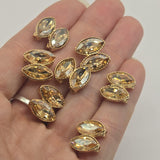 Package of six champagne rhinestone 2 hole slider beads in a polished bright gold finish. Each decorative bead measures approximately 13 mm wide and 15 mm tall, with 9 mm between the holes. Two faceted marquise-shaped champagne stones create a sparkling double-stone arrangement framed by textured gold settings. Perfect for handmade bracelets, necklaces, decorative cuffs, bead weaving, and elegant jewelry-making projects.