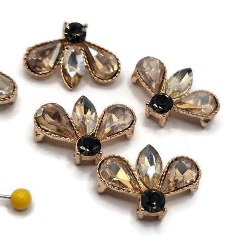 Close-up of bright gold smoked topaz rhinestone slider beads featuring a distinctive three-petal fan-shaped design. Two faceted light champagne teardrop rhinestones surround a pointed marquise-shaped center stone, while a dark round rhinestone accents the base. Detailed textured gold borders frame the sparkling stones, adding dimensional beauty to these decorative 2 hole focal beads for jewelry making.