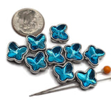 Nine electric blue butterfly 2 hole slider beads arranged on a white background. Each butterfly features a vibrant faceted blue stone with turquoise, aqua, and deep blue reflections surrounded by a polished platinum silver metal setting. These small decorative butterfly focal beads measure approximately 11 mm wide and 10.5 mm tall, perfect for handmade bracelets, necklaces, bead weaving, and multi-strand jewelry designs.