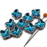 Detailed view of electric blue butterfly 2 hole slider beads with highly reflective faceted blue stones. The angular surfaces create brilliant flashes of turquoise, aqua, teal, and darker blue, giving each butterfly a sparkling dimensional appearance. Bright platinum silver settings frame the butterfly-shaped stones, creating colorful decorative components for handmade bracelets, necklaces, and jewelry-making projects.