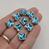 Electric blue butterfly 2 hole slider beads displayed with jewelry-making pins demonstrating their side-drilled construction. Each butterfly features a faceted electric blue stone surrounded by polished platinum silver metal, with approximately 5 mm between the holes. These decorative components help maintain strand spacing in double-strand bracelets, bead weaving, necklaces, and multi-strand handmade jewelry.