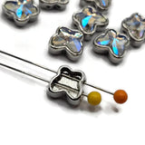 Close-up of platinum silver butterfly slider beads featuring sparkling Clear AB faceted stones. Each stone follows the shape of the butterfly wings, creating a dimensional design with reflective rainbow flashes. Polished platinum silver metal borders highlight the butterfly silhouettes, making these decorative 2 hole focal beads beautiful for jewelry making, bracelet designs, and bead weaving.