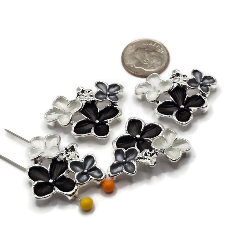 Four bright silver floral 2 hole slider beads arranged on a white background, each featuring a dimensional arrangement of black, smoky gray, and pearl white enamel flowers. The decorative floral focal beads measure approximately 30 mm wide and 23 mm tall with 11 mm between the holes. Polished silver outlines and delicate raised flower centers add beautiful detail for handmade bracelets, necklaces, and bead weaving.