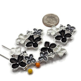 Four bright silver floral 2 hole slider beads arranged on a white background, each featuring a dimensional arrangement of black, smoky gray, and pearl white enamel flowers. The decorative floral focal beads measure approximately 30 mm wide and 23 mm tall with 11 mm between the holes. Polished silver outlines and delicate raised flower centers add beautiful detail for handmade bracelets, necklaces, and bead weaving.