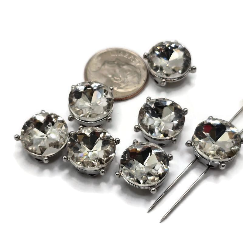 Seven platinum silver round 2 hole slider beads featuring large sparkling clear rhinestones arranged on a white background. Each decorative jewelry-making bead measures approximately 12 mm in diameter with 5 mm between the holes. The brilliant faceted stones are surrounded by polished stainless steel-colored silver metal settings with small raised prong accents, perfect for handmade bracelets, necklaces, and bead weaving.