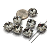 Seven platinum silver round 2 hole slider beads featuring large sparkling clear rhinestones arranged on a white background. Each decorative jewelry-making bead measures approximately 12 mm in diameter with 5 mm between the holes. The brilliant faceted stones are surrounded by polished stainless steel-colored silver metal settings with small raised prong accents, perfect for handmade bracelets, necklaces, and bead weaving.