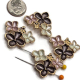 Pink, charcoal gray, and pearl white enamel floral slider beads displayed beside a US dime for size comparison. Each decorative 2 hole jewelry-making bead measures approximately 30 mm wide and 23 mm tall with 11 mm between the holes. The bright gold finish surrounds three dimensional enamel flowers, making these focal beads ideal for bracelets, necklaces, bead weaving, and decorative cuffs.