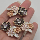 Elegant bright gold floral 2 hole slider beads featuring dimensional charcoal-black, soft pink, and peach enamel flowers accented with pearl white leaves and sparkling clear rhinestones. Each decorative focal bead measures approximately 32 mm wide and 19 mm tall with 8 mm between the holes. Three floral jewelry-making beads per package for handmade bracelets, necklaces, botanical accessories, decorative cuffs, and bead weaving.