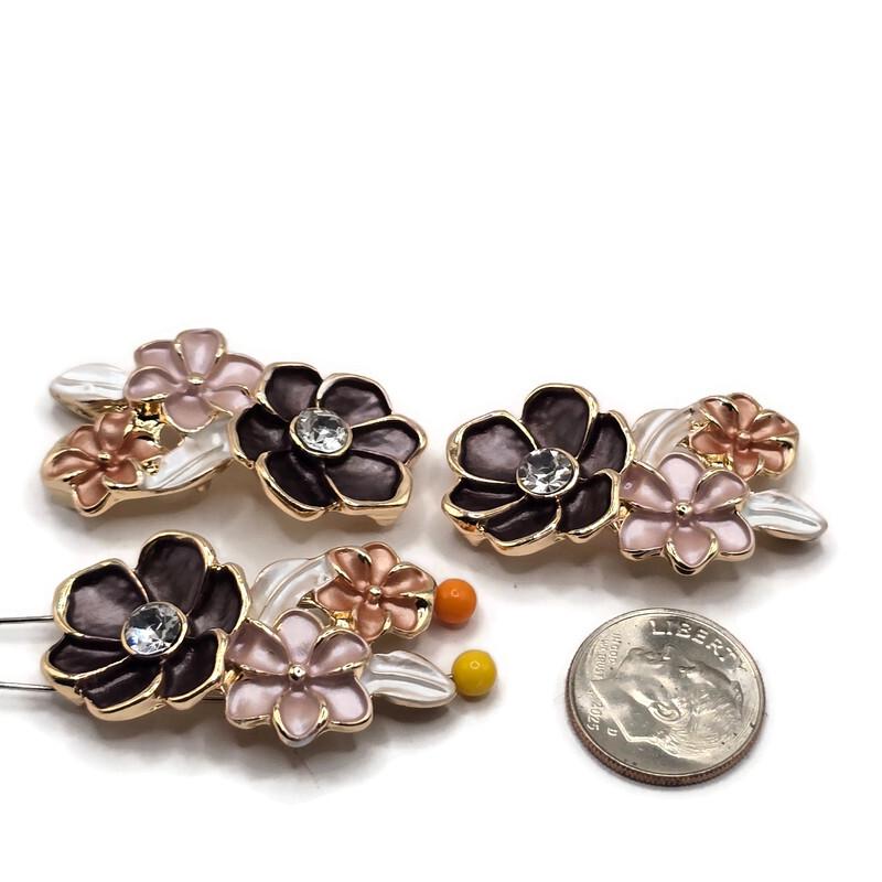 Three bright gold floral 2 hole slider beads arranged on a white background, each featuring dimensional charcoal-black, soft pink, and peach enamel flowers with pearl white leaves. A sparkling clear rhinestone accents the center of the larger dark flower. Each decorative jewelry-making focal bead measures approximately 32 mm wide and 19 mm tall with 8 mm between the holes, perfect for handmade bracelets, necklaces, and bead weaving.