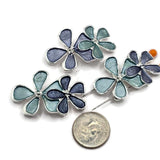 Stunning floral 2 Hole Slider Beads featuring overlapping five-petal flowers in complementary aqua blue, slate blue, and dusty blue enamel finishes. Bright reflective silver metalwork outlines each decorative petal, while raised silver centers add delicate detail. These beautiful jewelry focal beads are perfect for handmade bracelets, beaded necklaces, multi-strand jewelry, and creative bead weaving. Versatile jewelry making supplies for designers colorful flowers and elegant silver accents.