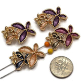 Beautiful gold floral focal beads featuring contrasting purple, burgundy, champagne, peach, and charcoal blue enamel flowers. Each decorative jewelry component showcases three overlapping blossoms with elongated textured petals, polished gold borders, and delicate openwork metallic flower accents. These 2 Hole Slider Beads are perfect for handmade jewelry designs, multi-strand bracelets, necklace making, and bead weaving.