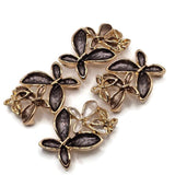 Beautiful charcoal gray and champagne floral 2 Hole Slider Beads featuring three overlapping flowers with textured smoky gray, soft taupe, and pearly ivory enamel petals. Each decorative jewelry focal bead showcases highly reflective bright gold outlines and delicate openwork gold flower accents. These elegant jewelry components are perfect for handmade bracelets, necklace designs, bead weaving, and multi-strand jewelry.