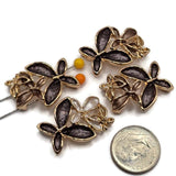 Stunning charcoal gray Flower Slider Beads featuring an artistic arrangement of overlapping enamel blossoms accented with highly polished bright gold metalwork. The coordinated package includes deep smoky gray flowers paired with warm champagne, taupe, and pearly ivory accents. These dimensional floral jewelry focal beads are ideal for handmade bracelets, beaded necklaces, multi-strand jewelry, and creative bead weaving.