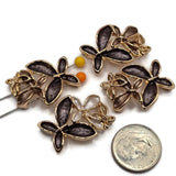 Decorative charcoal gray and champagne 2 Hole Slider Beads featuring beautiful overlapping flowers with textured enamel petals and reflective bright gold outlines. The neutral color combinations include smoky charcoal, warm taupe, soft champagne, and pearly ivory accents. Each jewelry focal bead includes a delicate openwork gold flower for additional dimensional detail.