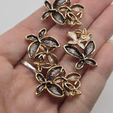 Elegant bright gold flower jewelry making beads featuring layered floral designs with contrasting charcoal gray, smoky champagne, taupe, and ivory enamel petals. Each 2 Hole Slider Bead showcases a large dark gray flower paired with smaller neutral blossoms and delicate metallic floral accents. Beautiful jewelry components for bracelet making, necklace designs, bead weaving, and handmade accessories.