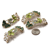 Beautiful bright gold butterfly and floral 2 Hole Slider Beads featuring dimensional emerald green and lime green butterflies surrounded by delicate white and sage green flowers. Each butterfly showcases textured enamel wings outlined in polished gold, while the flowers feature detailed gold centers. These elongated botanical focal beads are perfect for handmade bracelets, necklaces, bead weaving, decorative cuffs, and nature-inspired jewelry designs featuring vibrant green accents.