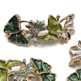 Four beautiful bright gold butterfly and flower 2 Hole Slider Beads featuring vibrant green enamel wings and delicate floral accents. Each elongated focal bead showcases contrasting dark emerald and light lime green butterflies, complemented by white and sage green flowers with detailed gold centers. The dimensional openwork design creates a delicate botanical appearance for handmade bracelets, necklaces, decorative cuffs, and creative bead-woven jewelry.