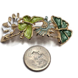 Detailed view of a bright gold butterfly jewelry focal bead featuring two beautifully sculpted green butterflies connected by delicate flowers and curved gold stems. Rich dark green and fresh lime green enamel wings showcase textured surfaces, while soft white and sage flowers add elegant contrast. These decorative 2 Hole Slider Beads bring botanical charm and vibrant color to handmade bracelets, necklaces, bead weaving, and nature-inspired jewelry.