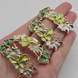 Close-up of an intricate green butterfly and floral slider bead featuring rich emerald green and bright lime green enamel butterflies with sculpted wing details. Delicate white and soft sage green flowers with textured gold centers connect the butterflies in an elegant botanical arrangement. Polished bright gold outlines emphasize the dimensional design. These decorative 2 Hole Slider Beads are ideal for handmade bracelets, necklaces, bead weaving, and garden-inspired accessories.