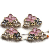 Beautiful bright gold floral 2 hole slider beads featuring three dimensional enamel flowers in soft pink, smoky gray, and pearl white. Each decorative bead showcases one larger pink flower with textured petals and two smaller coordinating flowers with polished gold outlines. Tiny raised gold centers and decorative gold accents complete the arrangement. Perfect for handmade bracelets, necklaces, bead weaving, and romantic floral jewelry designs.