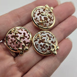 Close-up of bright gold pastel enamel filigree slider beads featuring delicate circular openwork designs and raised gold flowers. The decorative beads showcase soft blush pink, pearl white, and silvery gray enamel with subtle textured detailing. Polished gold outlines frame the intricate cutout patterns, creating a beautiful combination of color, shine, and dimension for double-strand bracelets, necklaces, bead weaving, and handmade jewelry.