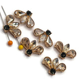 Detailed view of light smoked topaz rhinestone 2 hole slider beads in polished bright gold settings. The faceted teardrop and marquise rhinestones reflect warm champagne, pale amber, and golden tones, beautifully contrasted by a dark smoked topaz round rhinestone. The unusual fan-shaped arrangement creates a sparkling floral-inspired focal bead for handmade bracelets, necklaces, and multi-strand jewelry.