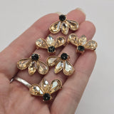 Unique fan-shaped floral rhinestone slider beads measuring approximately 22 mm wide and 15 mm tall. Three outward-facing faceted light smoked topaz stones form a decorative fan arrangement, accented by a contrasting dark round rhinestone at the base. Polished bright gold settings with textured edging add warmth and detail to these distinctive 2 hole jewelry-making focal beads.