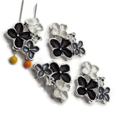 Black, gray, and pearl white enamel floral slider beads displayed beside a US dime for size comparison. Each decorative 2 hole jewelry-making bead measures approximately 30 mm wide and 23 mm tall with 11 mm between the holes. The bright silver finish surrounds three dimensional enamel flowers, making these focal beads ideal for bracelets, necklaces, bead weaving, and decorative cuffs.