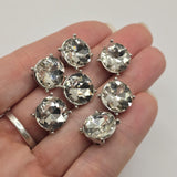 Close-up of clear rhinestone round 2 hole slider beads in a polished platinum silver finish. Each bead features a large faceted clear rhinestone surrounded by a smooth silver-toned metal setting with four decorative raised prong-style accents. The sparkling stones reflect light beautifully, creating elegant focal beads for handmade bracelets, necklaces, and decorative bead-woven jewelry.