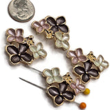 Four bright gold floral 2 hole slider beads arranged on a white background, each featuring a dimensional arrangement of dusty pink, charcoal gray, and pearl white enamel flowers. The decorative floral focal beads measure approximately 30 mm wide and 23 mm tall with 11 mm between the holes. Polished gold outlines and delicate raised flower centers add beautiful detail for handmade bracelets, necklaces, and bead weaving.