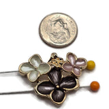 Detailed view of bright gold floral 2 hole slider beads featuring contrasting dusty pink, charcoal gray, and pearl white enamel flowers. The larger charcoal-gray flower has softly textured petals, while the smaller flowers display delicate pink and luminous pearlescent white finishes. Polished gold outlines and raised floral centers create a beautiful botanical jewelry-making focal bead.